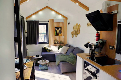 Charmante tiny house in Nederland met lichte woonkamer, keuken, grijze bank en sfeervolle wanddecoratie.
