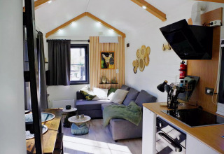 Acogedora tiny house en Países Bajos con sala, cocina pequeña, sofá gris y moderna decoración interior.