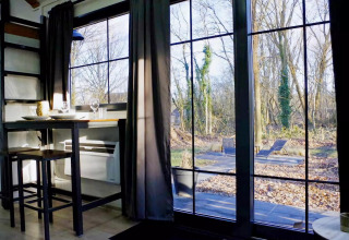 Vista desde el interior del Charming Tiny House en Países Bajos, con mesa, sillas y ventanales al bosque.
