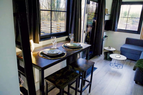 Knusse woon- en eethoek in Charming Tiny House in Nederland met gedekte tafel en hoge ramen.