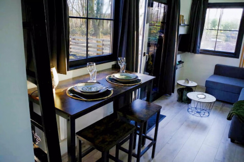 Acogedora sala-comedor en el Charming Tiny House de Países Bajos, con mesa puesta y grandes ventanas.