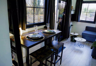 Acogedora sala-comedor en el Charming Tiny House de Países Bajos, con mesa puesta y grandes ventanas.