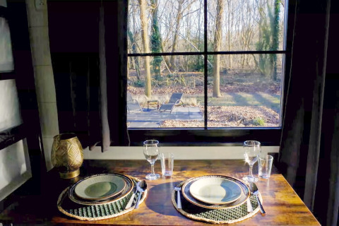 Sfeervol gedekte tafel voor twee bij het raam met boszicht in Charming Tiny House, Nederland.