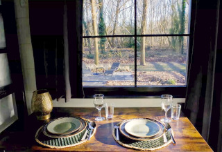 Sfeervol gedekte tafel voor twee bij het raam met boszicht in Charming Tiny House, Nederland.