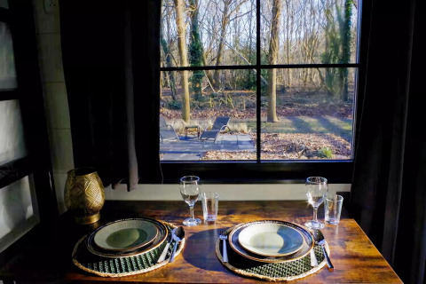 Mesa elegantemente puesta para dos junto a una ventana con vistas al bosque en Charming Tiny House, Países Bajos.