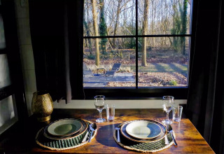 Mesa elegantemente puesta para dos junto a una ventana con vistas al bosque en Charming Tiny House, Países Bajos.