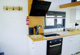 Cocina moderna en Charming Tiny House, Países Bajos, con campana negra, horno y gran ventana.
