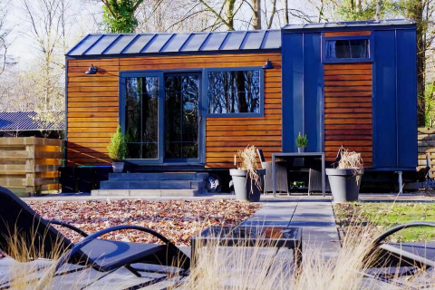Casa pequeña moderna con revestimiento de madera y grandes ventanales en un jardín en los Países Bajos.