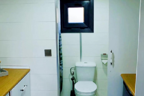 Baño en una tiny house en los Países Bajos con inodoro, pequeña ventana, portarrollos y encimeras de madera.