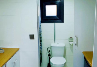 Baño en una tiny house en los Países Bajos con inodoro, pequeña ventana, portarrollos y encimeras de madera.