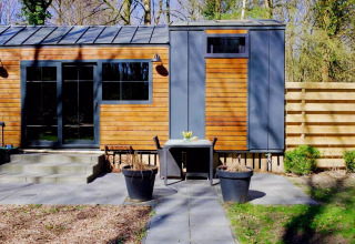 Charming Tiny House en Países Bajos con fachada de madera, terraza, mesa al aire libre y plantas verdes.