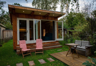 Gezellig houten chalet in Sint Maartenszee met open deuren, terrasstoelen en groene omgeving.