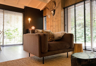 Moderne lodge woonkamer met bruine fauteuil, houten wanden en grote ramen in Dutch Cabin Houses C66.