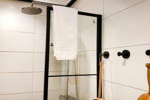 Moderne douche met zwart frame, witte handdoek en grote witte tegels bij Dutch Cabin Houses C66 in Nederland.