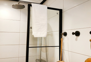 Moderne douche met zwart frame, witte handdoek en grote witte tegels bij Dutch Cabin Houses C66 in Nederland.