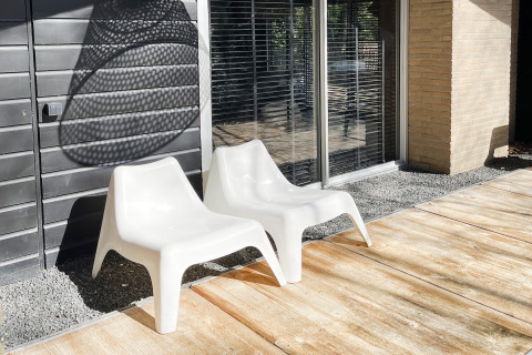 Twee witte stoelen op een zonnig terras bij grote ramen van Dutch Cabin Houses C66 in Nederland.
