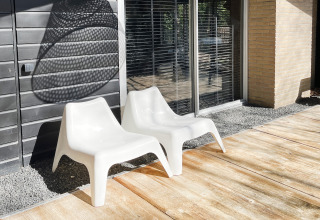 Twee witte stoelen op een zonnig terras bij grote ramen van Dutch Cabin Houses C66 in Nederland.