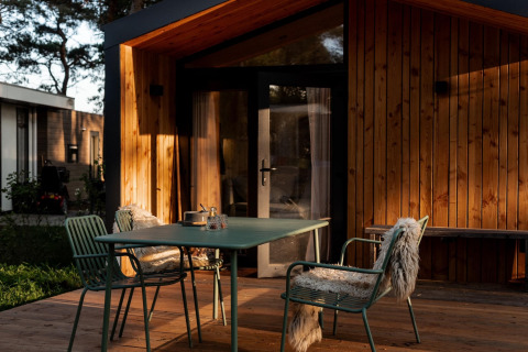 Zona de comedor exterior con sillas verdes y mesa sobre terraza de madera en Haarle, Países Bajos.