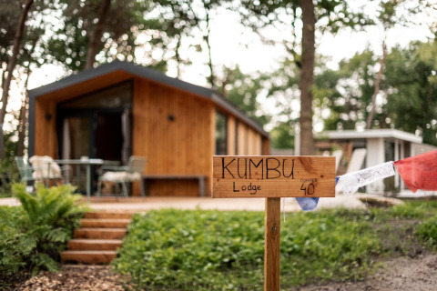 Træhytte med skilte, hvor der står 'Kumbu Lodge', omgivet af træer nær Sallandse Heuvelrug i Holland.