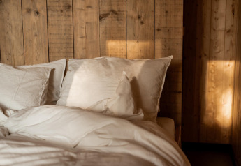 La luz del sol entra en un dormitorio acogedor con pared de madera y almohadas blancas en una cabaña en Haarle.