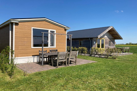 Twee stijlvolle lodges met buitenterras op een groene weide onder een blauwe lucht in Nederland.