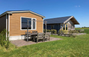 Twee charmante lodges met buitenzitje op een groene grasmat onder blauwe lucht in Nederland.