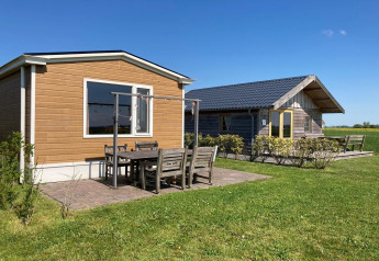 Twee charmante lodges met buitenzitje op een groene grasmat onder blauwe lucht in Nederland.
