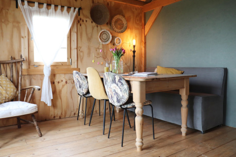 Knusse eetruimte in een Nederlandse lodge met houten tafel, diverse stoelen, manden en zachte verlichting.