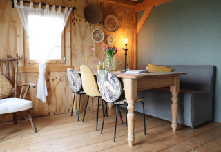 Knusse eetruimte in een Nederlandse lodge met houten tafel, diverse stoelen, manden en zachte verlichting.