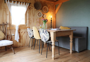 Gezellige eethoek in een Nederlandse lodge met houten tafel, diverse stoelen, manden en warme sfeer.