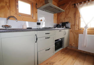 Moderne lodge keuken met groene kasten, fornuis, koffiezetapparaat en houten ramen in Frisian Hideaway.