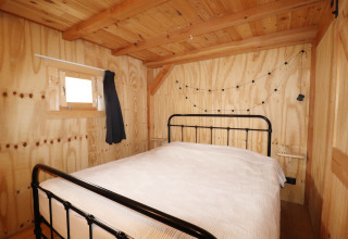 Sfeervolle slaapkamer met houten wanden, metalen bed en lichtsnoer in het Frisian Hideaway with Style in Nederland.