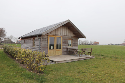 Knus houten huisje genaamd Frisian Hideaway with Style met veranda en bankje op het platteland.