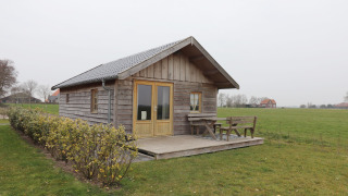Knus houten huisje genaamd Frisian Hideaway with Style met veranda en bankje op het platteland.