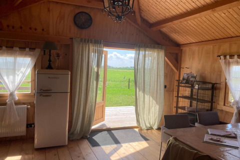 Houten lodge-interieur met open deuren, retro koelkast, gordijnen en uitzicht bij Frisian Hideaway.
