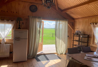 Houten lodge-interieur met open deuren, retro koelkast, gordijnen en uitzicht bij Frisian Hideaway.