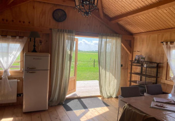 Knus houten lodge-interieur met open deuren, gordijnen, retro koelkast en uitzicht op het groen.