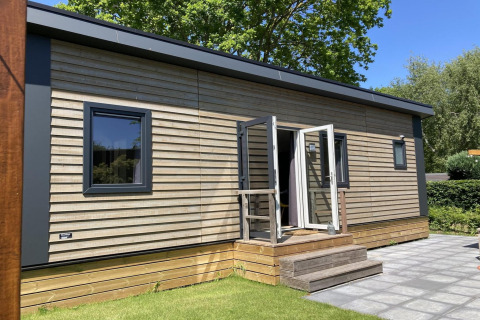 Modernes Chalet mit Holzverkleidung, Garten und Terrasse, sonnig gelegen, umgeben von Bäumen.
