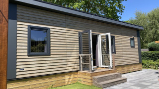 Modernes Chalet mit Holzverkleidung, Garten und Terrasse, sonnig gelegen, umgeben von Bäumen.