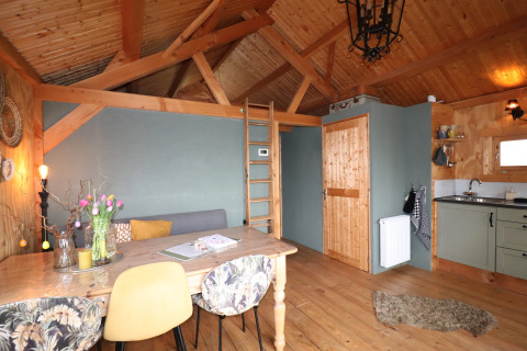 Knus lodge-interieur bij Frisian Hideaway met houten balken, eettafel, ladder en kleine keuken.