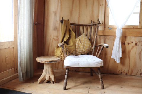 Knus hoekje met houten stoel, kussen, gele plaid en bijzettafel in een stijlvolle Nederlandse lodge.