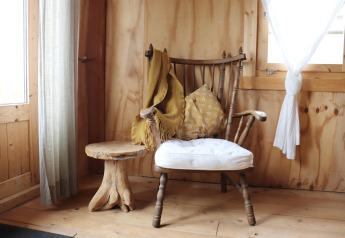 Gezellige hoek met houten stoel, kussen, gele plaid en bijzettafeltje in een stijlvolle lodge.