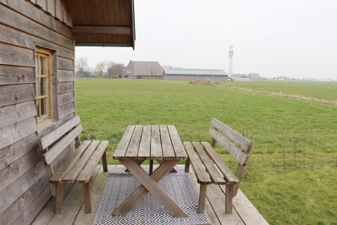 Houten banken en tafel op een veranda met uitzicht op een groen veld bij Frisian Hideaway with Style, Nederland.