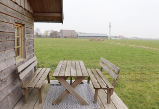 Houten banken en tafel op een veranda met uitzicht op een groen veld bij Frisian Hideaway with Style, Nederland.