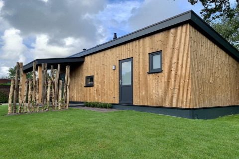 Modern chalet genaamd Pleasant met veranda, houten gevel, groene grasmat en bewolkte lucht.