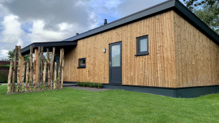 Modern chalet genaamd Pleasant met veranda, houten wandbekleding, gras en bewolkte lucht.