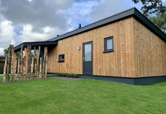 Chalet moderne appelé Pleasant avec véranda, extérieur en bois, pelouse verte et ciel nuageux.
