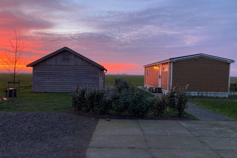 Zonsondergang bij twee houten lodges van Frisian Hideaway with Style in Nederland, met uitzicht op weilanden.