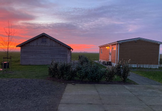 Zonsondergang bij twee houten lodges van Frisian Hideaway with Style in Nederland, met uitzicht op weilanden.