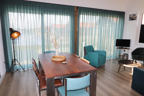 Luminoso interior de lodge en los Países Bajos con cortinas azuladas, mesa de madera y mobiliario moderno.